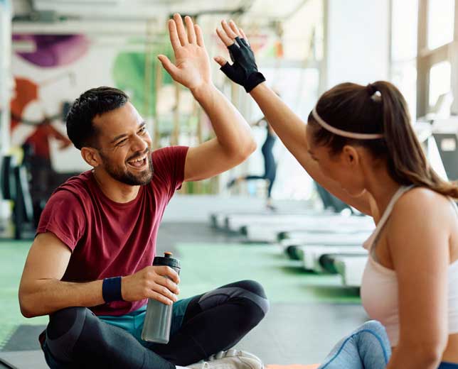 Consulta realizada correctamente Dos personas, un hombre y una mujer, sentados en el suelo de un gimnasio dándose un