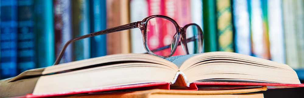 Imagen de una biblioteca con unos libros con unas gafas encima