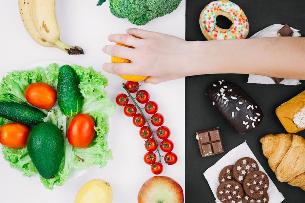 Mesa con verduras, dulces y una mano cogiendo una fruta