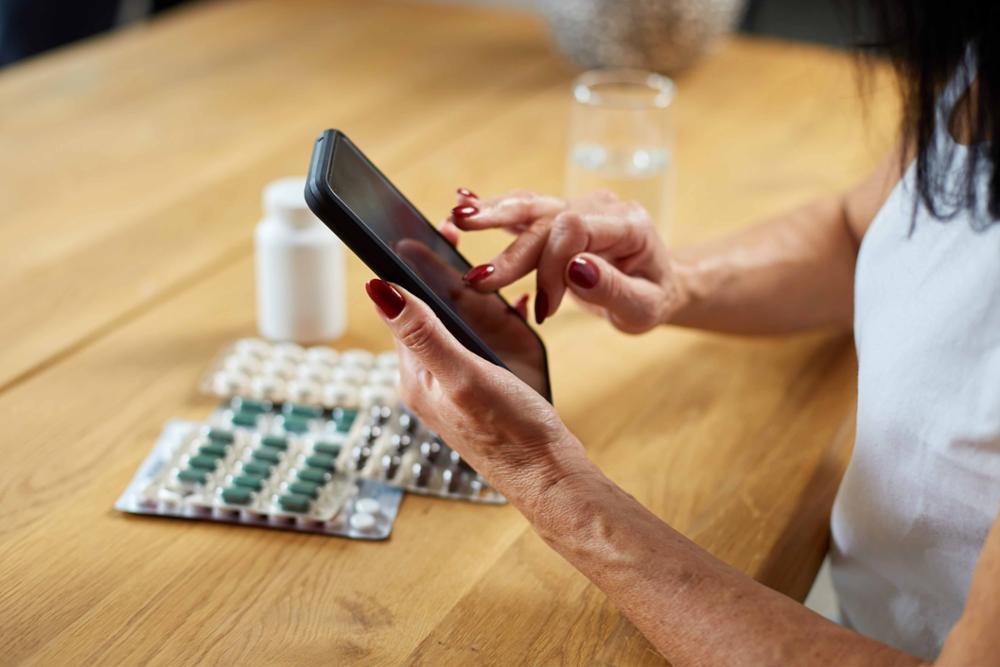 Mujer con un móvil consulta los prospectos de unas pastillas que tiene en la mesa