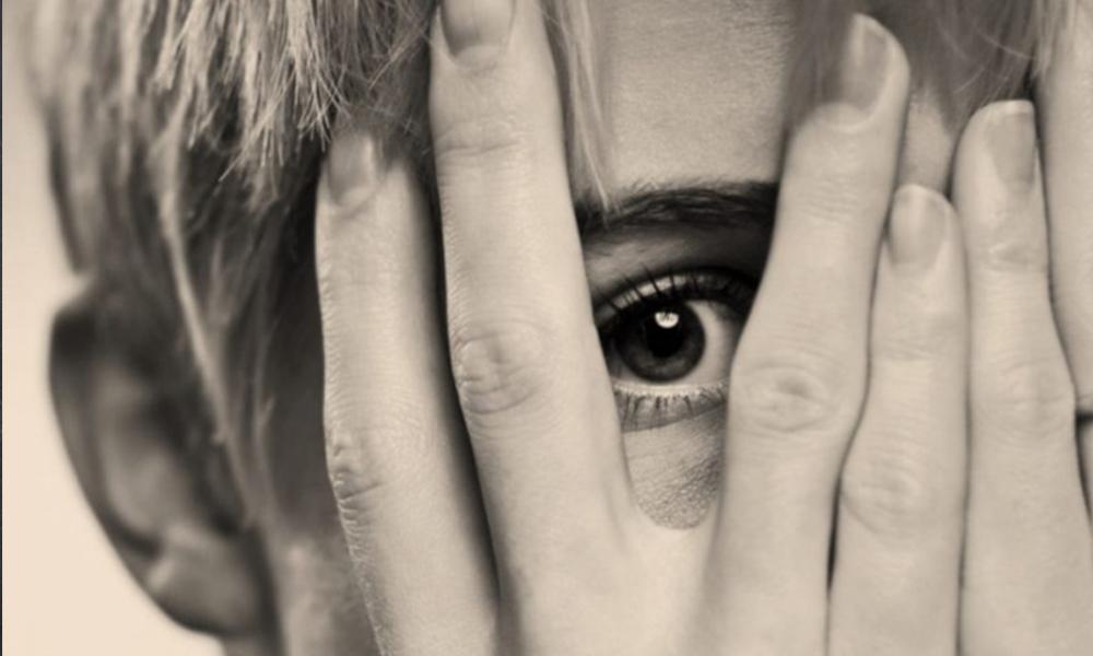 rostro de mujer que asoma timidamente entre los dedos de su mano