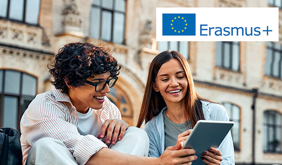 Dos jóvenes estudiantes, una chica y un chico, se ríen mientras miran una tablet con un paisaje de alguna ciudad europea detrás