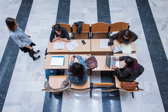 Estudiantes jóvenes sentados en mesa y sillas viendo tablets y portátiles