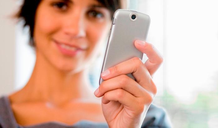 Imagen en la que aparece una mujer con un telefono móvil en la mano