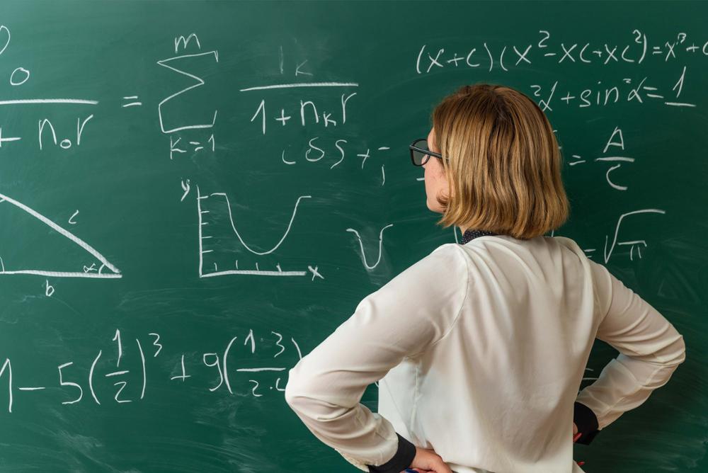 Profesora observando una pizarra llena de fórmulas matemáticas.