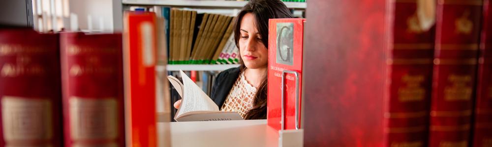 foto de chica en una biblioteca hojeando un libro entre las estanterias