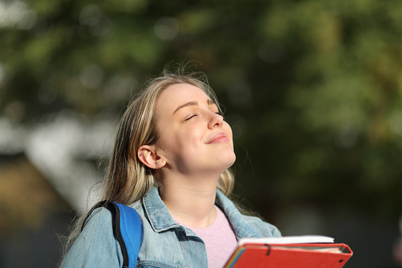 Chica respirando al aire libre con gesto de calma, en sus manos lleva una carpeta
